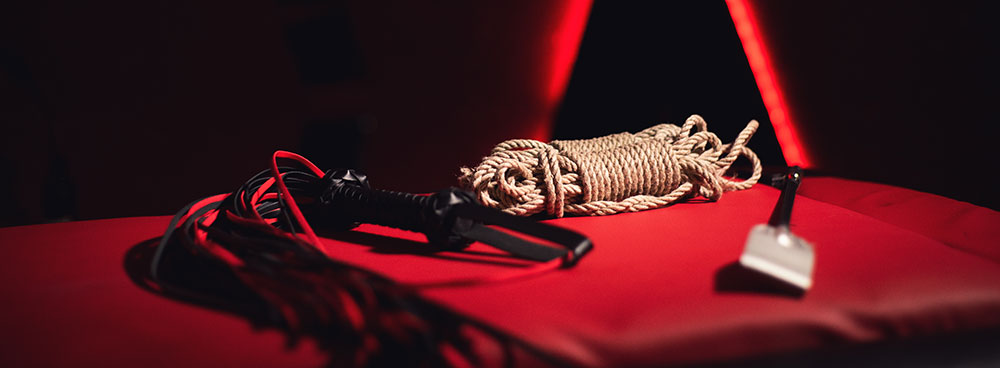 Flogger, SM-Gerte und Bondage-Rope auf rotem Tuch