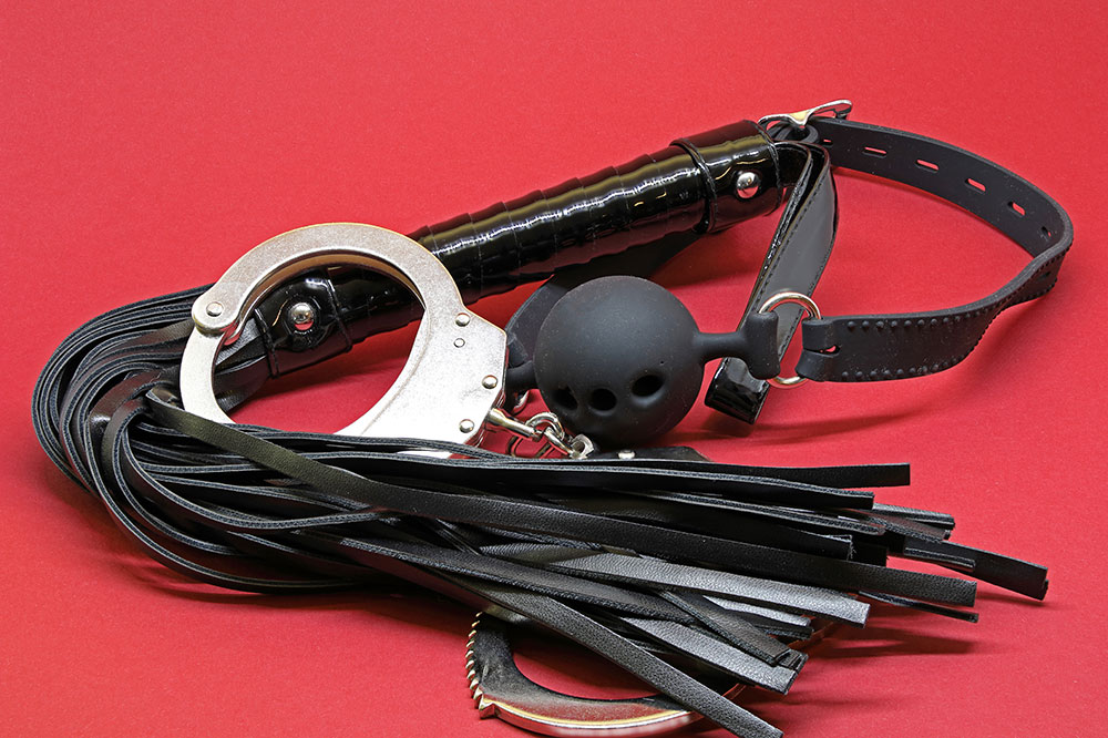 Flogger, Handschellen und Knebel auf rotem Hintergrund